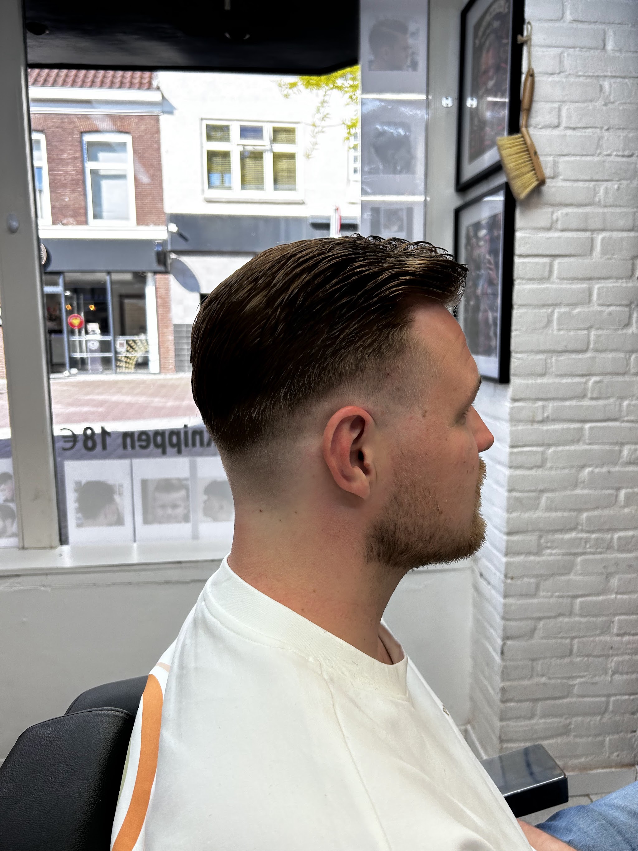 Klant met een afgewerkt kapsel bij het raam van Barber Fuat